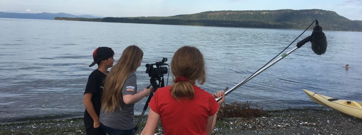 three youth on a beach filming a swimmer